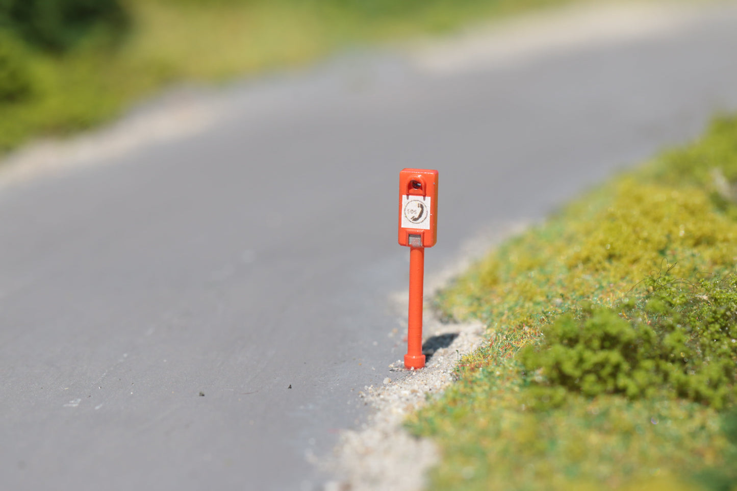 Eine maßstabsgetreue Notrufsäule von DorrModellbau an einer sommerlichen Landstraße im Maßstab H0 1:87.