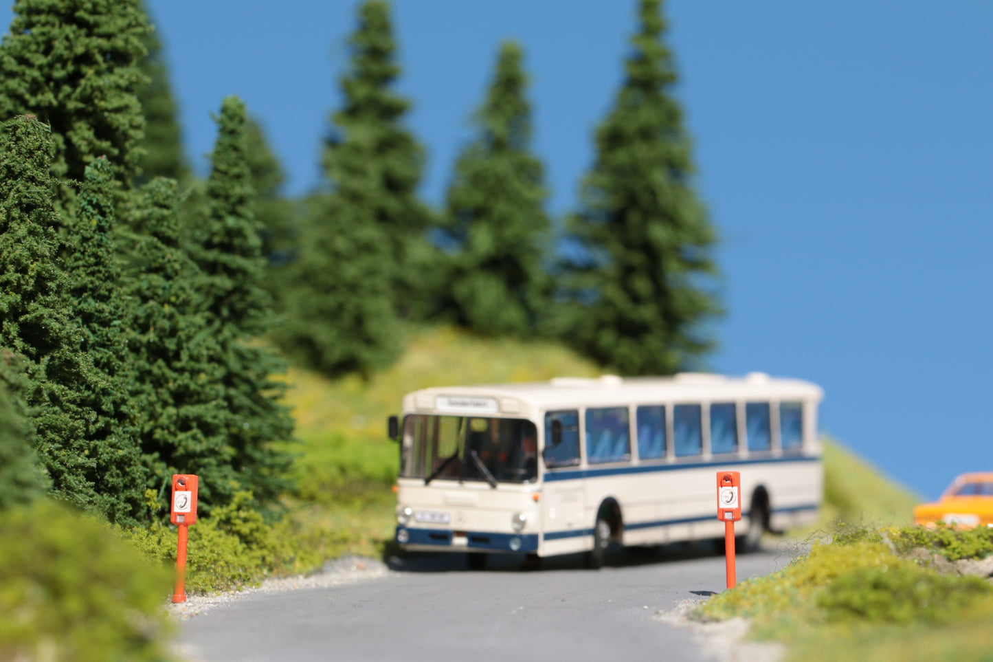 Auf einer Landstraße im Schwarzwald fährt ein Linienbus an zwei detaillierten Notrufsäulen im Maßstab H0 1:87 von DorrModellbau vorbei.