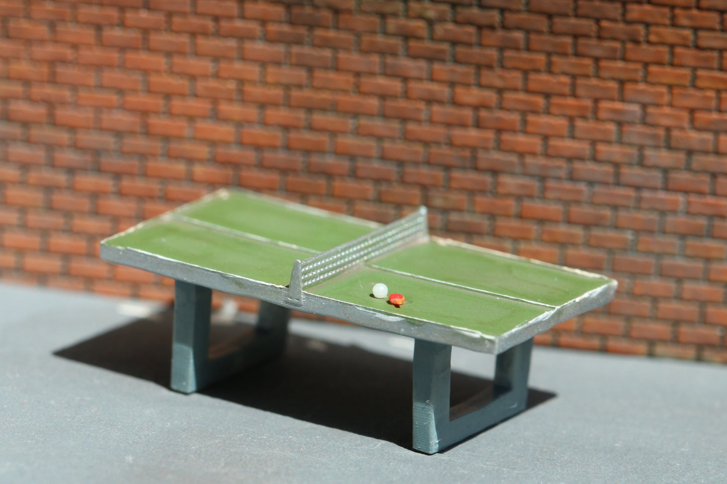 Eine detaillierte Tischtennisplatte im Maßstab H0 von DorrModellbau steht vor einer Backsteinwand