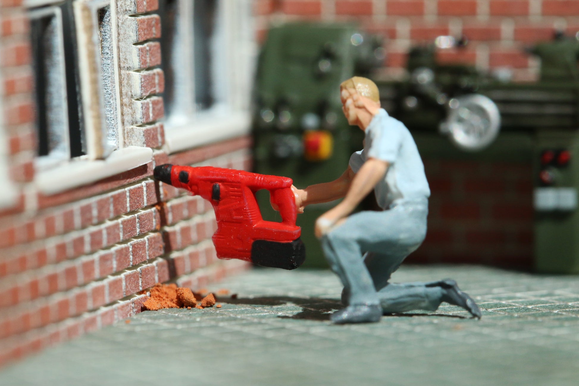 Ein Arbeiter bohrt mit einem Schlagbohrer von DorrModellbau im Maßstab 1:87 in eine Modell-Backsteinwand.
