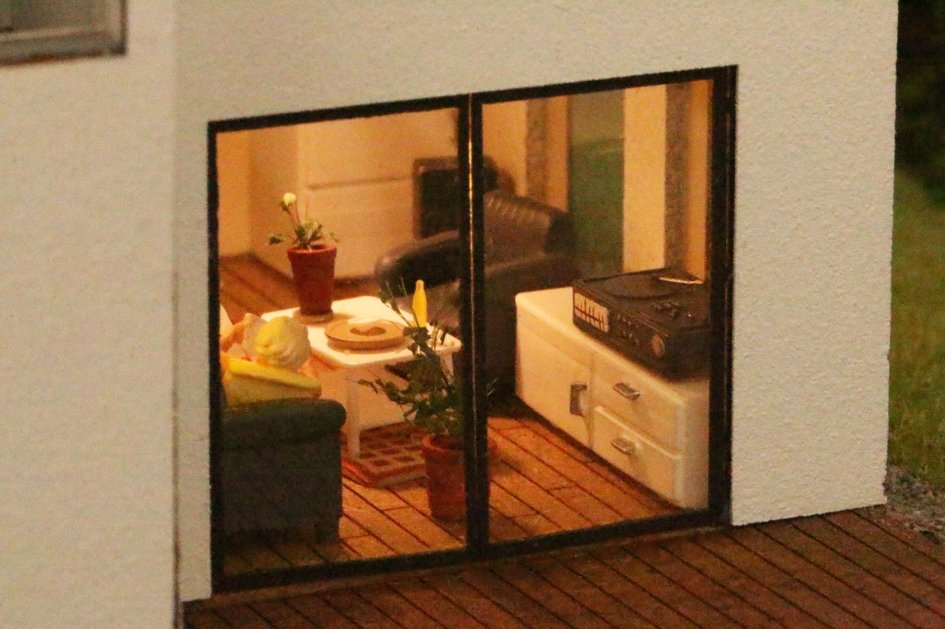 Durch das Fenster sieht man ins detailliert ausgestaltete Wohnzimmer eines Modellhauses.